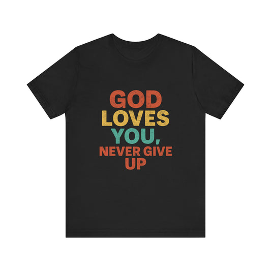 Young woman pointing to a bold black t-shirt with the words "God Loves You. Never Give Up," holding a white "Klippette" cap, standing confidently in front of a gate.