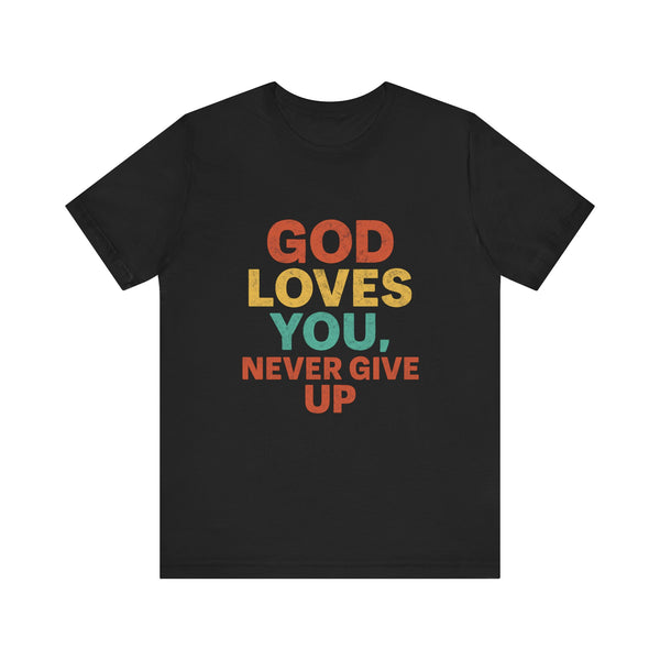 Young woman pointing to a bold black t-shirt with the words "God Loves You. Never Give Up," holding a white "Klippette" cap, standing confidently in front of a gate.