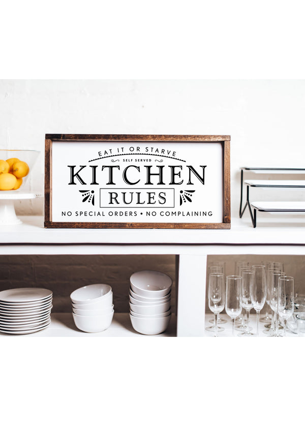 Rustic wooden kitchen sign with bold black lettering that reads: “Kitchen Rules – Eat it or starve. No complaining. No special orders.”
